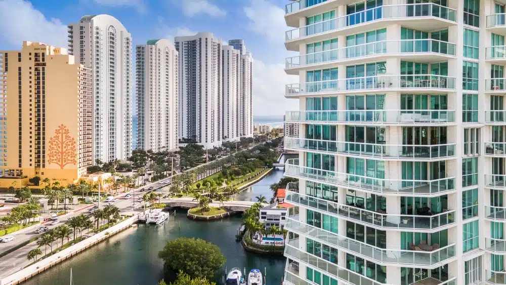 Row of tall modern apartment buildings beside a canal with a pedestrian bridge and boats rare in the waterway.