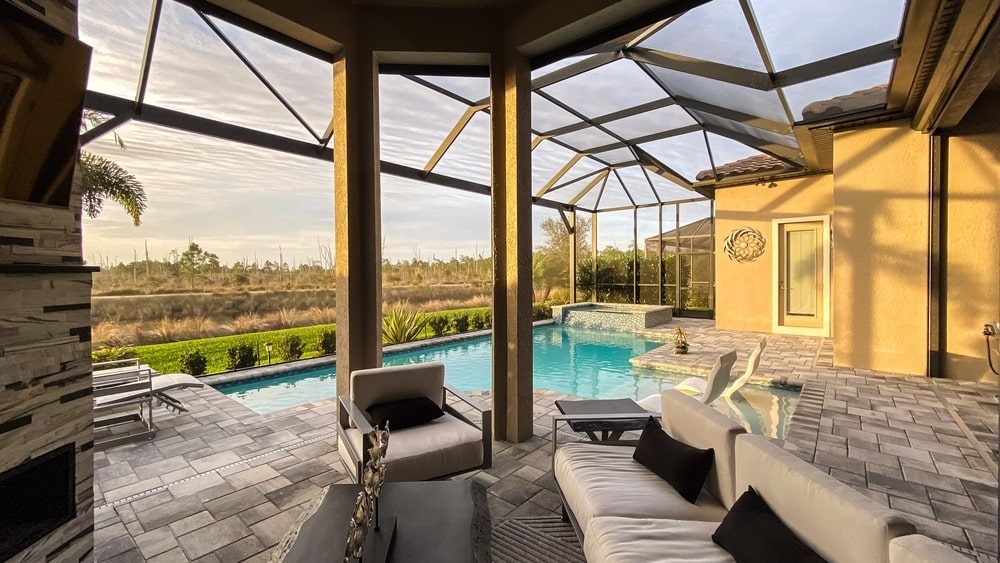 Patio with a glass-enclosed pool area, modern seating, and a desert landscape at sunset.